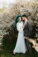 a bearded groom plays and a girl with green hair against the background of blooming spring photo