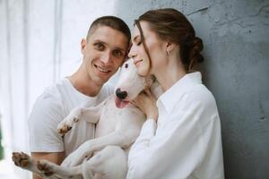 young couple guy and girl in a bright room playing with pet photo