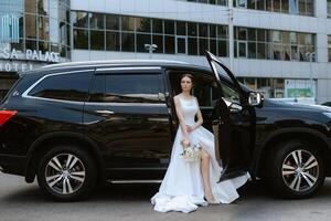 bride with a black car near a glass skyscraper photo