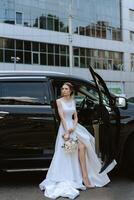 bride with a black car near a glass skyscraper photo