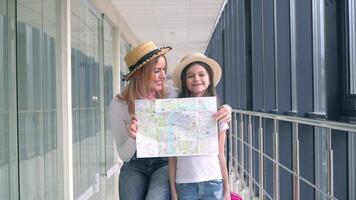 Beautiful woman with little girl holding a tourist map at the airport. Woman with daughter covers faces with tourist map video