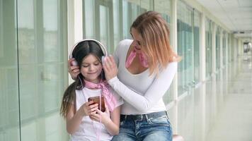 mamá toma cuidado de su hija a el aeropuerto poniendo en su auriculares. esperando vuelo video