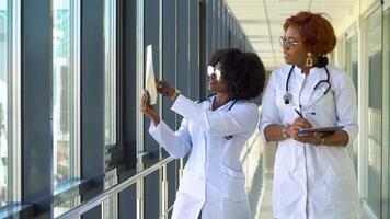 Two female african-american doctors examines x-ray of lungs, holding it in hands indoors. Two specialists holds transparent image of chest in arms, and carefully researches it video