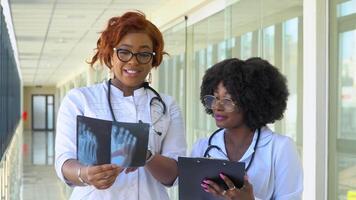 Two female african-american doctors examines x-ray of leg, holding it in hands indoors. Two specialists holds transparent image of leg in arms, and carefully researches it video