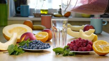 Raspberry Blueberry Melon Smoothie is poured into a glass on the background of fresh fruits and berries. The fruit cocktail is ready to eat. Healthy and vegetarian food concept video