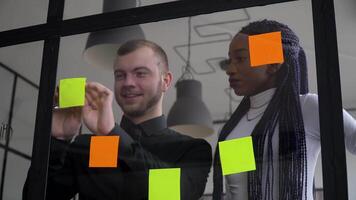 Corporate business multiethnic people using sticky notes, solving strategy on glass whiteboard. Team leader male showing solution for project deadline in office meeting video