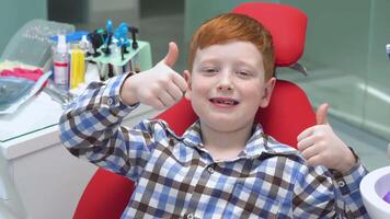 Lycklig rödhårig pojke på de tandläkare, närbild av liten pojke som visar tumme upp. pediatrisk tandvård video
