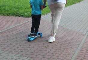 Sankt petrsburgo Rusia - 08 15 2023 madre ayuda su hijo paseo con patada scooter. contento familia madre enseña niño hijo a paseo un scooter en el parque. apoyo infancia paternidad idea. foto
