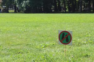 A sign of green color prohibiting walking on the territory of the meadow against the background of green grass. A sign standing on the grass and forbidding a person to stand on the grass. photo