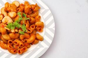 Macaroni Pasta with Tomato Sauce and Sliced Sausage Served on a white plate on a blue background. photo