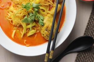 Northern Thai food Khao Soi, Spicy curry noodles soup with coconut milk and chicken drumstick, Local Thai food, Table top view photo