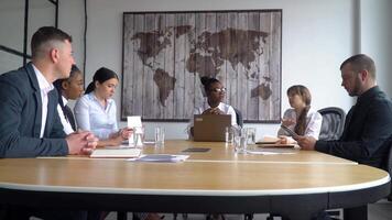 Diverse staff gathered together at briefing sit at table, african american employee takes part group discussion produce ideas and ways of solving problems, offering possibilities video