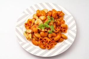 macarrones pasta con tomate salsa y rebanado salchicha servido en un blanco plato en un azul antecedentes. foto