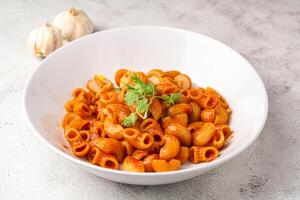 Macaroni with tomato sauce and parsley in a white bowl Served on a white plate photo