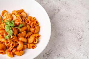 Macaroni with tomato sauce and parsley in a white bowl Served on a white plate, top view photo