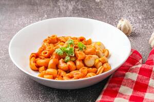 Macaroni with tomato sauce and parsley in a white bowl Served on a white plate photo
