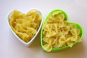 Butterfly shaped pasta stacked in a heart shape on the table. photo