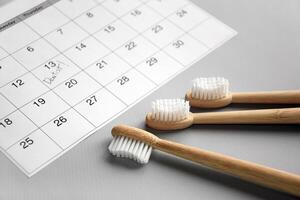 On a light gray background, there is a calendar with a dentist's note and toothbrushes. photo