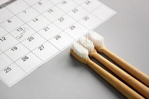 On a light gray background, there is a calendar with a dentist's note and toothbrushes. photo