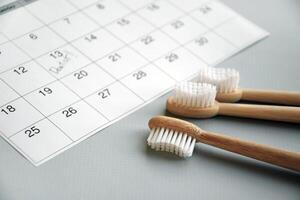 On a light gray background, there is a calendar with a dentist's note and toothbrushes. photo