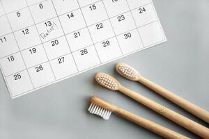 On a light gray background, there is a calendar with a dentist's note and toothbrushes. photo