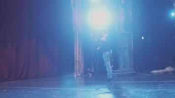 Ballet dancer in training suit practices visual moves on theater stage and prepares to performance. Dancer on choreography rehearsal before show. Illuminated theatrical hall. video