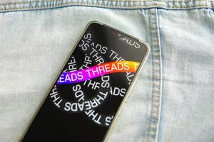 Tver, Russia - July 15, 2023, the threads logo on the smartphone screen lying on the jeans. The threads icon. The logo of the current application. Threads social network. photo