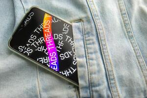 Tver, Russia - July 15, 2023, the threads logo on the smartphone screen lying on the jeans. The threads icon. The logo of the current application. Threads social network. photo