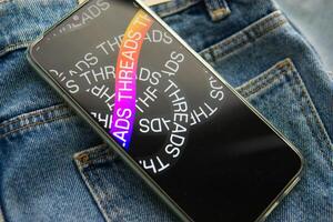 Tver, Russia - July 15, 2023, the threads logo on the smartphone screen lying on the jeans. The threads icon. The logo of the current application. Threads social network. photo