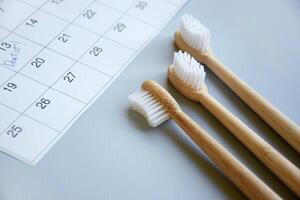 On a light gray background, there is a calendar with a dentist's note and toothbrushes. photo