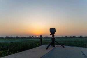 Tripod on Wooden Platform Near Field, A tripod stands on a wooden platform, placed beside an expansive field. photo