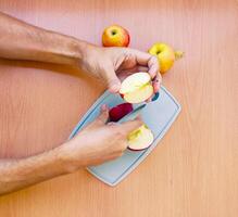Close up male hands cut an apple into slices. Top view of preparing fruits over kitchen table. photo