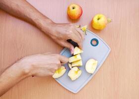 Close up male hands cut an apple into slices. Top view of preparing fruits over kitchen table. photo