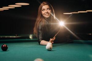 A girl with a cue in her hands makes a shot at a ball in a billiard club.Russian billiards photo