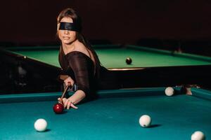 A girl with a blindfold and a cue in her hands in a billiard club.Russian billiards photo