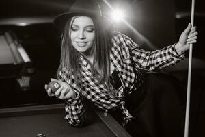 A girl in a hat in a billiard club with a cue and balls in her hands.Playing pool, black and white photo