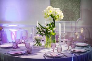 decoration of a festive dinner with flowers of lilies and tulips on the wedding table in the interior of the restaurant. Decorated table for a celebration in purple tones photo