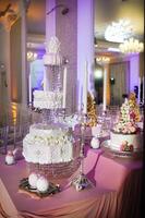 White three tiered wedding cake decorated with cream flowers on a stand photo