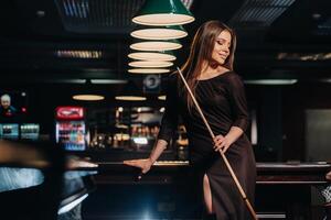 A girl in a hat in a billiard club with a cue in her hands.Pool Game photo