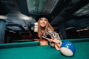 un niña en un sombrero en un de billar club con un señal en su manos golpes un pelota.jugando piscina foto