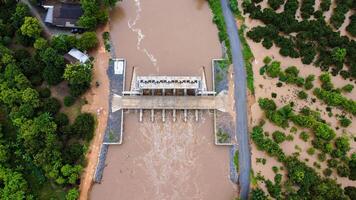 Aerial view of water released from the drainage channel of the concrete dam is a way of overflowing water in the rainy season. Top view of turbid brown forest water flows from a dam in Thailand. photo