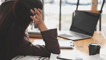 las mujeres asiáticas están estresadas mientras trabajan en una laptop, una mujer de negocios asiática cansada con dolor de cabeza en la oficina, se siente enferma en el trabajo, copia espacio video