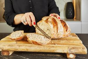 Landlady slicing bread on wooden board in marble kitchen with knife in hands photo