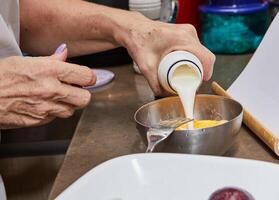 Chef's hands pouring cream into a bowl with mixture for cooking at home kitchen photo