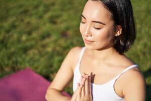 retrato de joven consciente de mujer, práctica yoga, hacer ejercicio, inhalar y exhalar en Fresco aire en parque, sentado en caucho estera foto