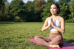 Woman meditating on lawn in park, sitting on sports mat, relaxing, breathing fresh air photo