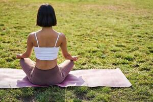 posterior ver de joven mujer meditando en Mañana parque, relajante, respiración práctica y bienestar formación sesión foto