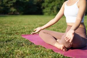 cuerpo de mujer meditando en parque, disfrutando el Dom vigas en su piel, relajante en aptitud formación en Mañana foto