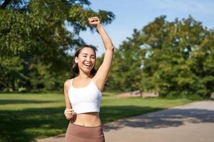 Hooray, victory. Smiling asian girl triumphing, celebrating achievement, running till finish, shouting from excitement photo