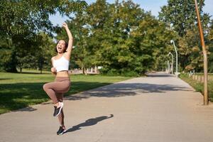 Excited young asian woman winning, finish running in park, saying yes, lifting hand up in triumph, celebrating victory or success photo